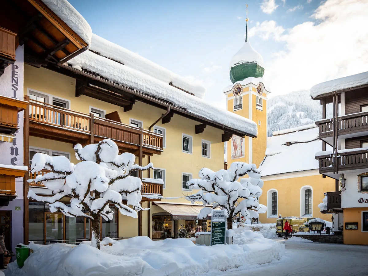Winterlandschaft mit schneebedeckten Bäumen, traditioneller Architektur und einem Kirchturm.